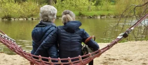 2 women sitting in a hammock which is near a lake